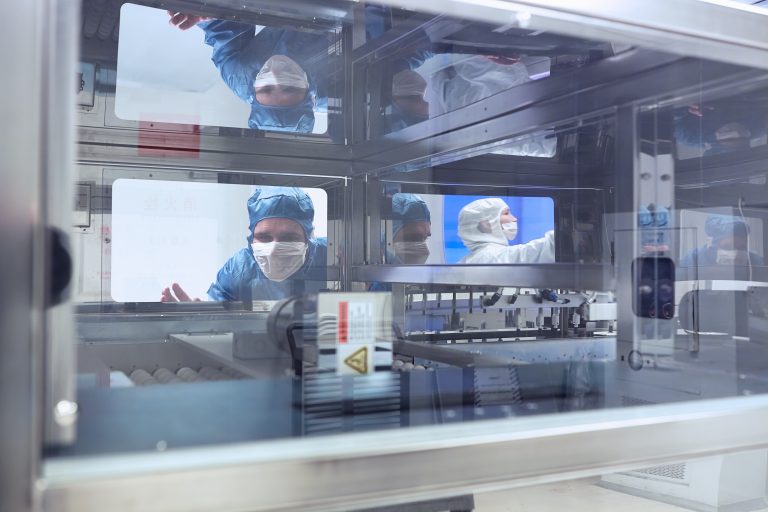 Male worker looking through manufacturing machine window in flexible electronics factory clean room
