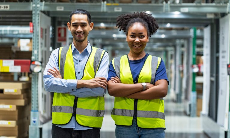 Asian male and African American female employee with arms crossed proudly serving in a furniture wholesale warehouse.
